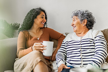 a daughter sitting on the couch with her mom having coffee